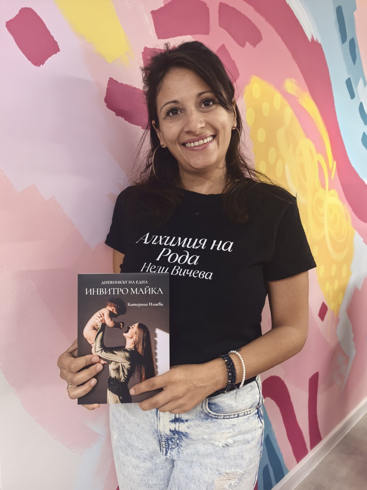 Читателка с книгата „Дневникът на една ИНВИТРО майка“ пред цветна стена